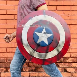 May include: A red, white, and blue Captain America shield with a five-pointed star in the center. The shield is made of metal and has a distressed look. UK Nautical Shop LTD is printed on the shield.