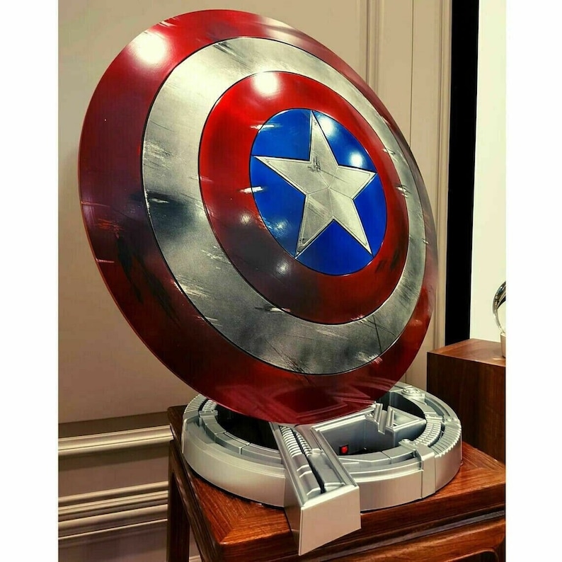 May include: A red, white, and blue Captain America shield with a distressed finish. The shield is mounted on a silver stand with a circular base.