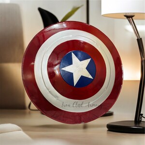 Pu&ograve; includere: Uno scudo di Capitan America rosso, bianco e blu con una stella a cinque punte al centro. Lo scudo ha un bordo argentato e le parole "Iron Clad Armory" sono stampate in basso.