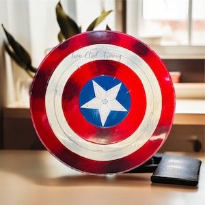 Pu&ograve; includere: Uno scudo di Capitan America rosso, bianco e blu con il testo "Iron Clad Armory" in alto. Lo scudo &egrave; fatto di un materiale plastico duro e ha una stella in rilievo al centro.