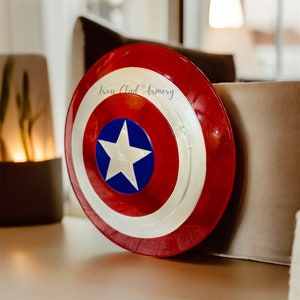 Pu&ograve; includere: Uno scudo di Capitan America rosso, bianco e blu con una stella bianca su sfondo blu. Lo scudo ha un bordo argentato e il testo "Iron Clad Armory" &egrave; visibile sullo scudo.