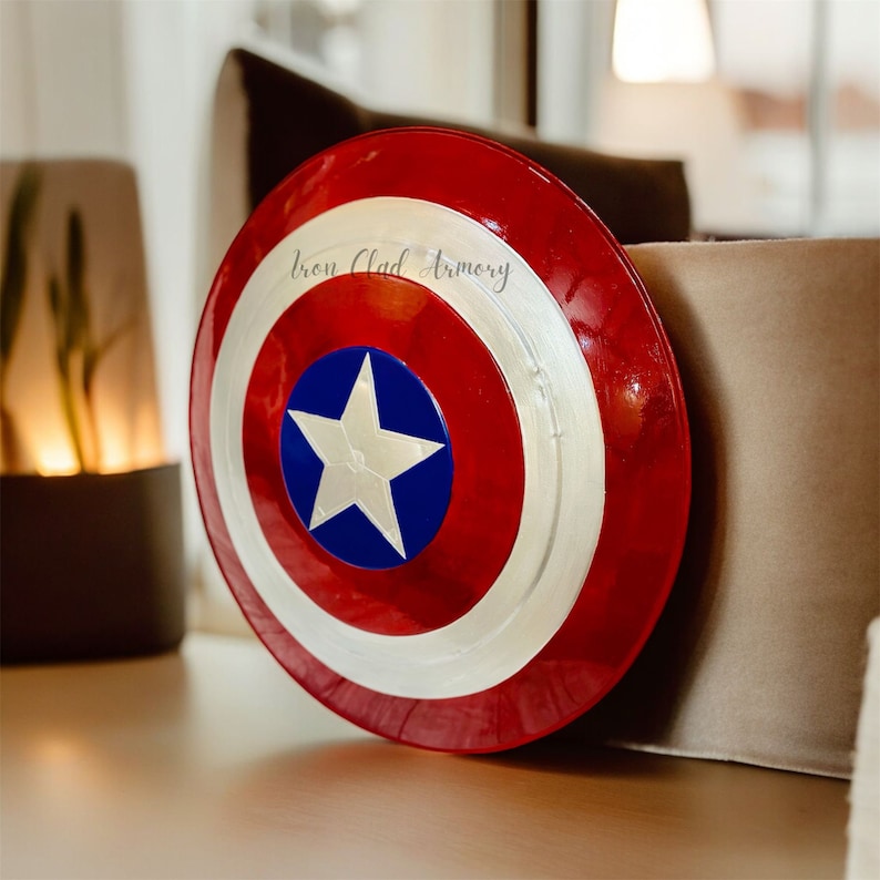 Pu&ograve; includere: Uno scudo di Capitan America rosso, bianco e blu con una stella bianca su sfondo blu. Lo scudo ha un bordo argentato e il testo "Iron Clad Armory" &egrave; visibile sullo scudo.