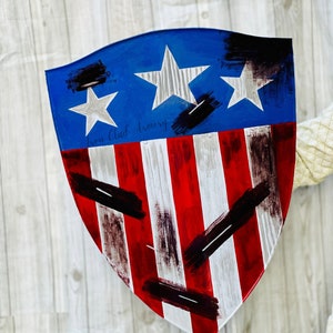 May include: A red, white, and blue shield with a distressed paint finish. The shield has three white stars on a blue background and the text "Ironclad Armory" is written in black.
