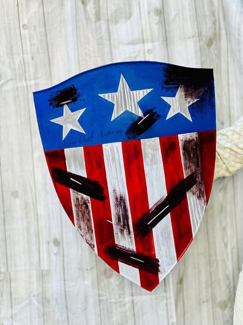 May include: A red, white, and blue shield with a distressed paint finish. The shield has three white stars on a blue background and the text "Ironclad Armory" is written in black.