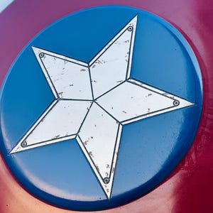 K&ouml;nnte beinhalten: Nahaufnahme eines rot-wei&szlig;-blauen Schildes mit einem wei&szlig;en f&uuml;nfzackigen Stern in der Mitte. Der Stern hat einen abgenutzten, alten Look und ist von einem blauen Kreis umgeben.