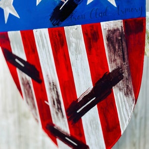 May include: A red, white, and blue shield with black paint splatters. The shield is shaped like a heart and has the text "Iron Clad Armory" written on it.