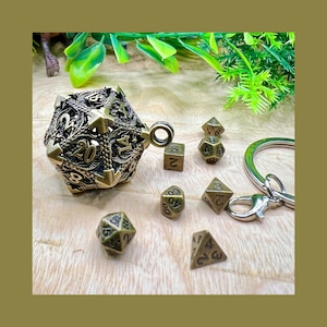 Può includere: Una collezione di dadi color ottone antico, tra cui un grande dado a venti facce ornato con un anello portachiavi. Diversi dadi più piccoli di varie forme sono sparsi, suggerendo un tema di gioco da tavolo.