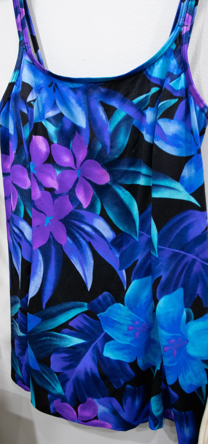 Puede incluir: Un ba&ntilde;ador negro con estampado tropical con flores y hojas azules, moradas y turquesa.