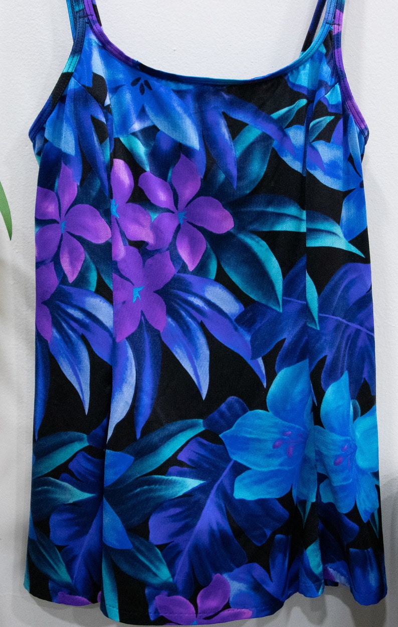 Puede incluir: Un ba&ntilde;ador negro con estampado tropical con flores y hojas azules, moradas y verde azulado.
