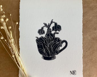 May include: Black and white linocut print of a bouquet of flowers in a teacup. The flowers are stylized and the teacup has a handle. The artist's initials "MK" are in the bottom right corner.