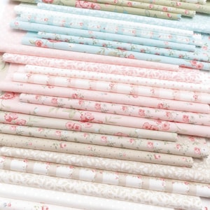 May include: A stack of folded fabric in various floral patterns and colors. The fabrics include shades of pink, blue, green, and beige, with designs featuring roses, dots, and stripes. The fabrics are likely cotton or a similar material.