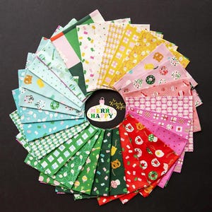May include: A circular arrangement of colorful fabric squares, each with a unique holiday-themed pattern. The fabrics feature gift boxes, ornaments, and other festive designs in shades of green, red, pink, and yellow. The center has a white oval with the words "Merry Happy".
