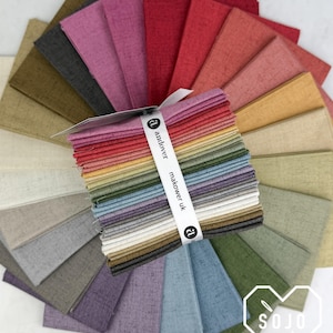 May include: A stack of square fabric swatches arranged in a fan pattern, featuring a variety of solid colors with a textured, linen-like appearance. A white paper band wraps around the center, printed with the text andover makower uk.