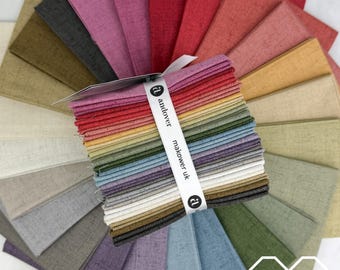 May include: A stack of square fabric swatches arranged in a fan pattern, featuring a variety of solid colors with a textured, linen-like appearance. A white paper band wraps around the center, printed with the text andover makower uk.