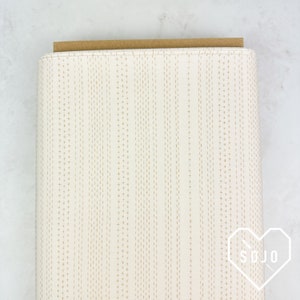 May include: A roll of white fabric with a subtle pattern of small gold plus signs arranged in vertical lines. The fabric is folded and the edge is visible.