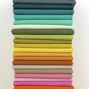 May include: A stack of folded fabric in various colors, ranging from blues and greens to yellows, oranges, and pinks. The fabric appears to be cotton or a similar material, with a smooth, even texture. The colors are vibrant and well-saturated.
