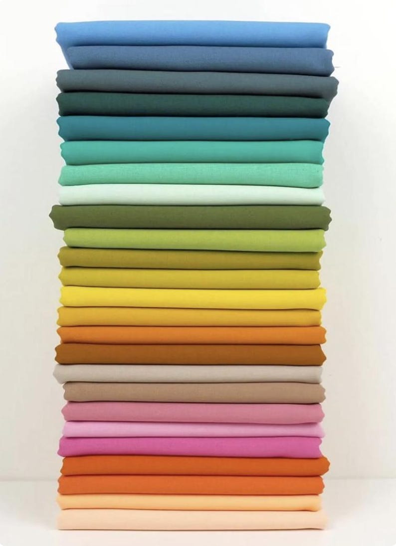 May include: A stack of folded fabric in various colors, ranging from blues and greens to yellows, oranges, and pinks. The fabric appears to be cotton or a similar material, with a smooth, even texture. The colors are vibrant and well-saturated.