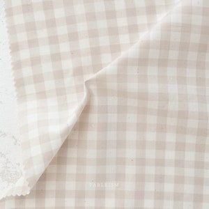 May include: A piece of beige and white gingham fabric. The fabric is folded, showing the pattern of evenly spaced squares. The edge of the fabric is visible, with a slightly uneven, cut edge. The word "FABLEISM" is printed in the bottom right corner.