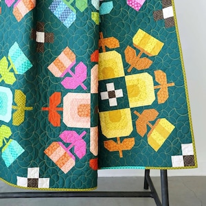 May include: A quilted blanket featuring a dark teal background with a repeating pattern of stylized flowers in shades of yellow, orange, pink, and light blue. The fabric displays a circular stitched texture and a border with small square accents.