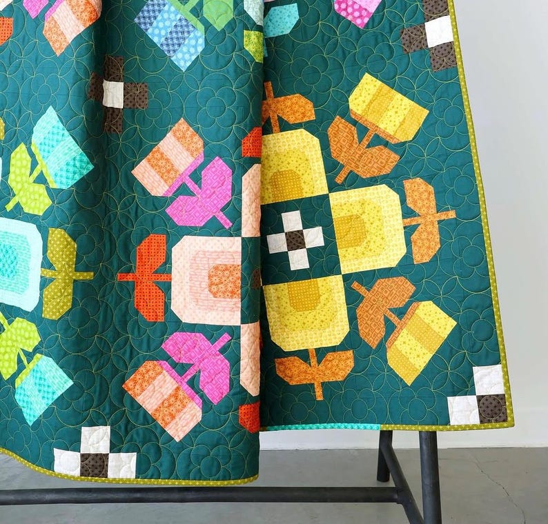 May include: A quilted blanket featuring a dark teal background with a repeating pattern of stylized flowers in shades of yellow, orange, pink, and light blue. The fabric displays a circular stitched texture and a border with small square accents.