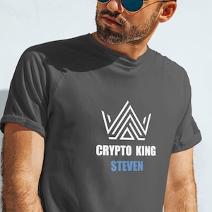 May include: A dark grey t-shirt with a white graphic of a crown and the text "CRYPTO KING STEVEN".