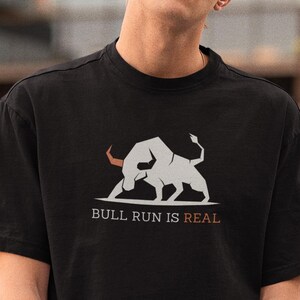 May include: Black t-shirt featuring a graphic of two bulls and the text "BULL RUN IS REAL" in white and orange. The shirt is a classic crew neck style.