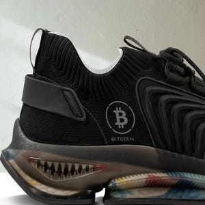 May include: Black athletic shoe with a white and black knit upper, a black sole, and a clear, multi-colored outsole. The shoe has a Bitcoin logo on the side with the text "Bitcoin".