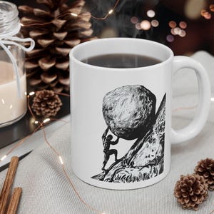 May include: White ceramic mug featuring a black and white illustration of a person pushing a large boulder up a mountain. The mug has a curved handle and is filled with a dark liquid. The design is a classic depiction of Sisyphus.