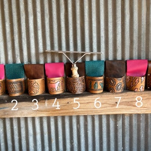 May include: Nine leather tool holders with different designs, including lightning bolts, a cow, a flower, and cacti. The holders are numbered 1 through 9.