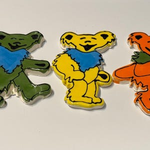 May include: Five ceramic figurines of dancing bears. The bears are each a different color: blue, green, yellow, orange, and pink. Each bear has a blue bandana around its neck.
