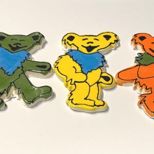 May include: Five flat, cutout bear figures arranged in a row. The bears are colored blue with a yellow chest, olive green with a blue chest, yellow with a blue chest, orange with a green chest, and light pink with a blue chest. Each bear has black outlines.