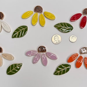 Può includere: Una collezione di tessere per mosaico in ceramica a forma di fiori e foglie nei colori bianco, giallo, rosso, beige, lavanda e arancione, con un centro marrone testurizzato. Include foglie verdi con venature bianche e due monete per scala.