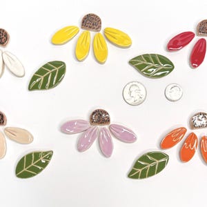 May include: A collection of ceramic flower and leaf mosaic tiles in white, yellow, red, beige, lavender, and orange, each with a brown textured center. Includes green leaves with white veins and two US coins for scale, measuring 0.95 and 0.71 inches.