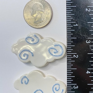 May include: Two white ceramic cloud-shaped ornaments with blue swirl designs. The clouds are approximately 2 inches in diameter.
