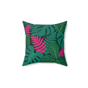 May include: Square cushion with a tropical leaf pattern. The design features large green monstera leaves, ferns, and pink accents on a dark background. The cushion is square and has a white background.