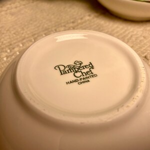 Puede incluir: Un cuenco de cer&aacute;mica blanco con el texto "The Pampered Chef HAND-PAINTED CHINA" impreso en negro. El cuenco es ligeramente curvado y parece nuevo.