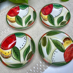 Puede incluir: Cuatro peque&ntilde;os cuencos de cer&aacute;mica pintados a mano. Cada cuenco presenta un interior blanco con un dise&ntilde;o de elementos rojos, amarillos y verdes, incluyendo hojas y frutas. Los bordes son verdes y los cuencos est&aacute;n dispuestos sobre una superficie de tono neutro.