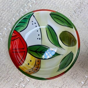 Puede incluir: Un cuenco de cer&aacute;mica pintado a mano con un colorido dise&ntilde;o de frutas y hojas. El cuenco presenta una paleta de colores rojo, verde, amarillo y blanco. El borde es verde con un acento rojo. El cuenco es adecuado para servir alimentos.