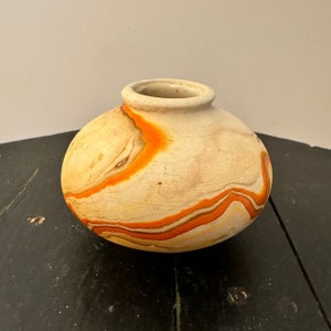 May include: A small, round, white ceramic vase with orange and brown swirling patterns.