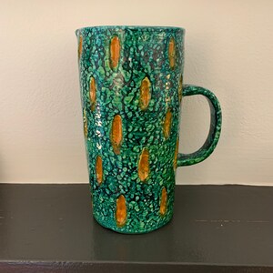 May include: A green ceramic pitcher with a speckled glaze and yellow accents. The pitcher has a handle and a wide mouth.