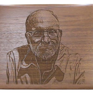 May include: A wood plaque with a laser engraved image of a man with a beard and glasses. The man is wearing a jacket and has a serious expression.