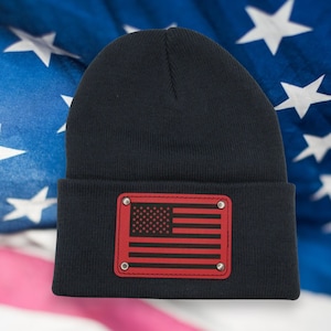 May include: A navy blue beanie with a red leather patch featuring a black and white American flag.