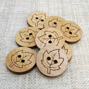 Peut inclure: Plusieurs boutons en bois avec un motif de feuille. Chaque bouton rond, d'environ 2,5 cm de diamètre, présente un motif de feuille découpé au laser avec deux petits trous pour la couture. Les boutons sont de couleur marron clair.