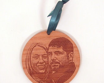 May include: A round wooden ornament with a laser-engraved image of a couple. The ornament is brown and has a green ribbon attached.