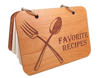 May include: A wooden recipe book with a ring binder. The cover is engraved with a fork and spoon crossed over each other and the words "Favorite Recipes".