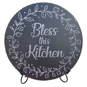 May include: A round black slate sign with a white floral design and the text "Bless this Kitchen". The sign is on a black metal stand.