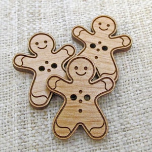 May include: Three wooden gingerbread man buttons with painted details. The buttons are light brown and have a smiling face, two eyes, and three buttons.