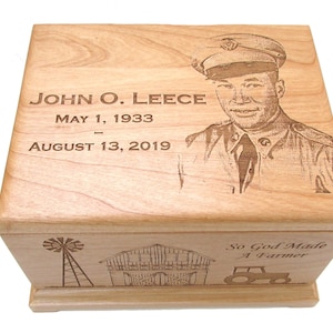 May include: A wooden cremation urn with a laser engraved image of a man in a military uniform. The urn also has the text "JOHN O. LEECE MAY 1, 1933 - AUGUST 13, 2019" and a scene of a farm with a windmill, barn, and tractor. The text "So God Made A Farmer" is also engraved on the urn.