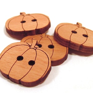 May include: Four wooden pumpkin-shaped buttons with a carved design. The buttons are a light brown color and have two holes each.