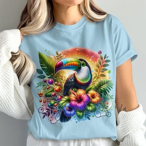 Pode incluir: Uma camiseta azul claro com uma estampa colorida de tucano e flores tropicais.